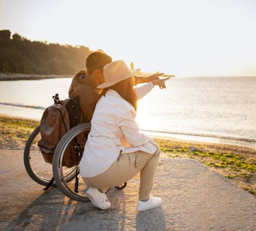 Couple enjoying sunset by the sea with wheelchair and NDIS Travel Support