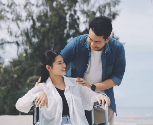 Smiling woman in wheelchair receiving NDIS travel assistance at the beach